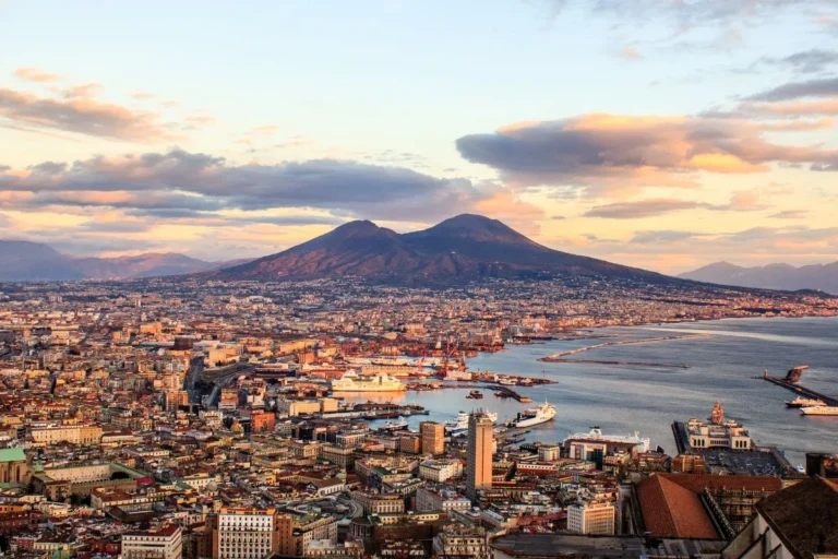 Veduta panoramica di Napoli con il Vesuvio sullo sfondo e il Golfo illuminato dal sole.