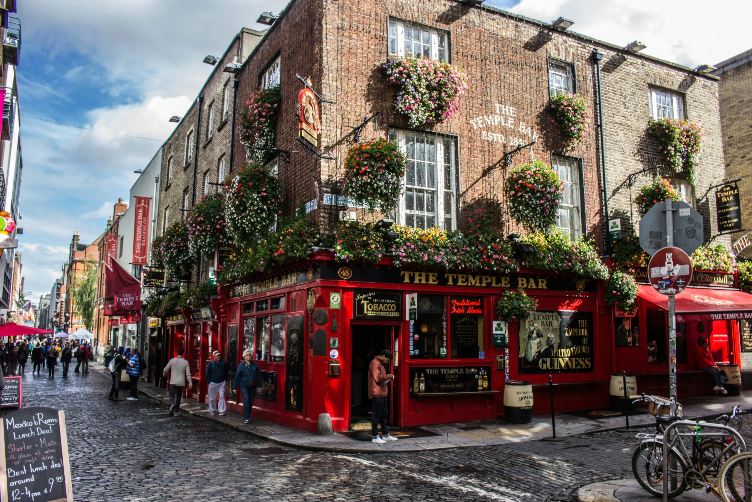 Facciata colorata del Temple Bar a Dublino, con insegne rosse, fiori e turisti all’esterno.